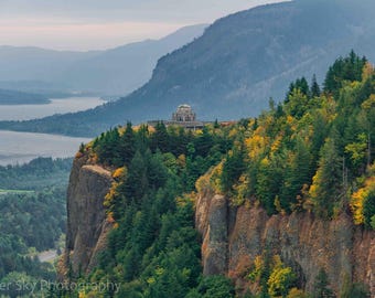 Puede incluir: Un paisaje escénico con un acantilado cubierto de árboles verdes y amarillos. Una estructura con forma de cúpula se encuentra en la cima, con vistas a un río y montañas distantes bajo un cielo nublado. Foto de Copper Sky Photography.