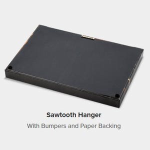 A black rectangular object with a metal hook on the top, labeled as a "Sawtooth Hanger" with "With Bumpers and Paper Backing".