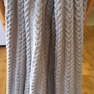 May include: A gray knitted cable knit throw blanket with a textured pattern.