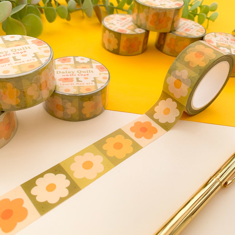 May include: A roll of green and yellow washi tape with a daisy pattern. The tape is labeled "Daisy Quilt Washi Tape Laurel Mae Art".