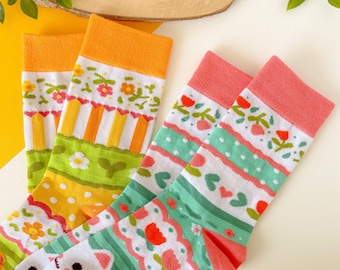 May include: Two pairs of colorful socks with a floral and geometric pattern. One pair is green, white, and pink with a floral pattern. The other pair is yellow, green, and white with a geometric pattern.