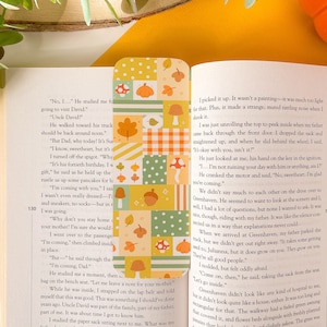 Puede incluir: Un marcapáginas con un diseño de patchwork que presenta hojas de otoño, bellotas y setas en tonos verdes, amarillos, naranjas y marrones. El marcapáginas está hecho de cartulina resistente y es perfecto para marcar tu lugar en un libro.