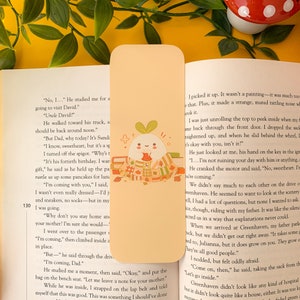 Op de afbeelding: Een bladwijzer met een schattig radijsje-personage dat een sjaal draagt en een kopje thee vasthoudt. Het personage wordt omringd door boeken, bladeren en eikels. De bladwijzer is gedrukt op een lichtoranje achtergrond met de tekst "No, 1... He studied me for a going to visit David." en "Uncle David?"