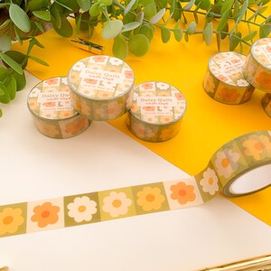 May include: Four rolls of green and orange floral patterned washi tape with the text "Daisy Quilt washi tape Laurel mas art" on each roll. One roll is unrolled and shows the pattern more clearly.