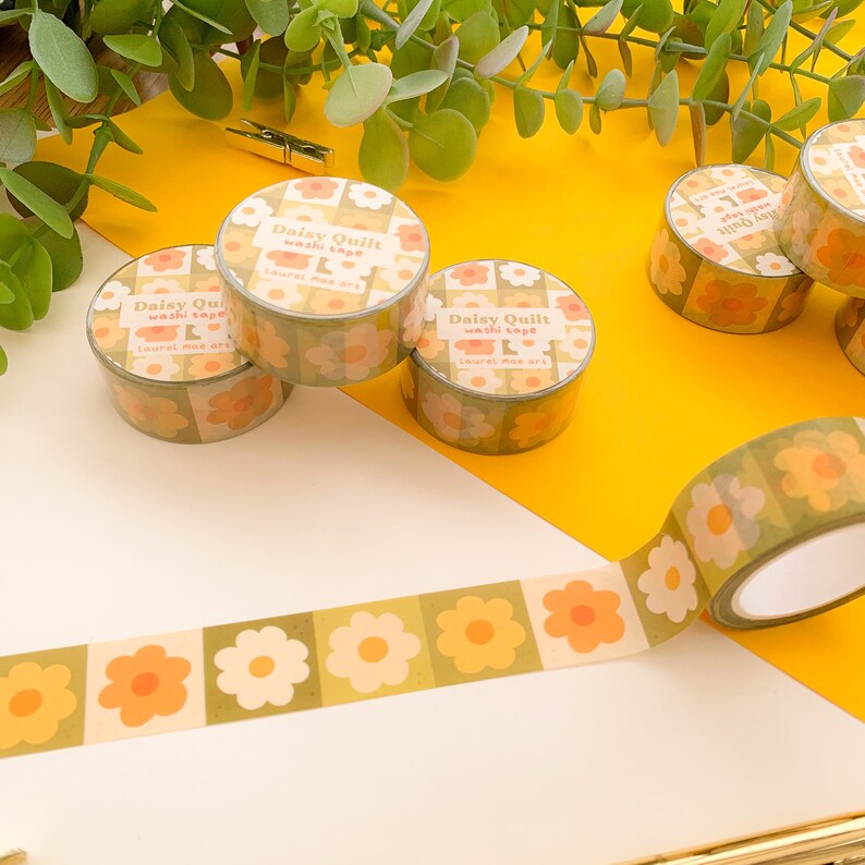 May include: Four rolls of green and orange floral patterned washi tape with the text "Daisy Quilt washi tape Laurel mas art" on each roll. One roll is unrolled and shows the pattern more clearly.
