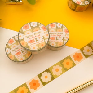 May include: Three rolls of washi tape with a daisy pattern. The tape is green and white with orange flowers. The tape is labeled "Daisy Quilt washi tape Laurel mae art".