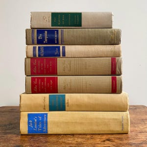 May include: A stack of vintage books with various titles and colors. The spines feature blue, red, and green labels with gold lettering. Titles include "The Making of Man," "The Turquoise," and "Tales of Adventure."