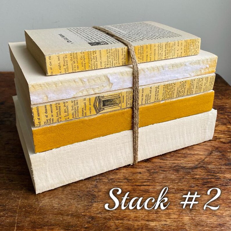 May include: A stack of five books with yellow and white covers. The books are tied together with twine. The top book has the text "The Food of Ancestry" on the cover. The text "Stack #2" is written on the wooden surface below the books.
