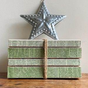 May include: A stack of four rectangular blocks wrapped with twine. The blocks are covered with pages from a vintage book, with green edges. A silver star hangs above the blocks.