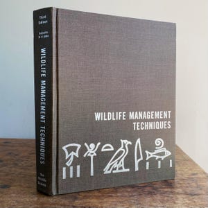 May include: A hardcover book titled "Wildlife Management Techniques" with a textured gray cover. The title and author's name are in white. The spine reads "Wildlife Management Techniques" vertically. The book is a third edition.