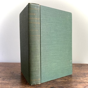 May include: A vintage hardcover book titled "UNDERSTANDABLE PSYCHIATRY" by Hinsie. The book has a green cover and spine with gold lettering. The book is standing upright on a wooden surface.