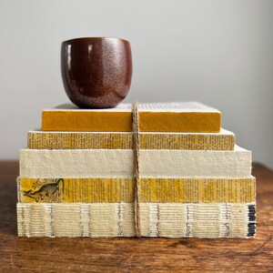 May include: A stack of vintage books with yellow and white covers, tied together with twine. A brown ceramic cup sits on top of the stack.