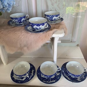 May include: Set of five blue and white porcelain teacups and saucers with a floral design. The cups and saucers are arranged on a white surface.