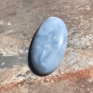 Puede incluir: Una piedra preciosa ovalada lisa de color azul claro con vetas blancas.