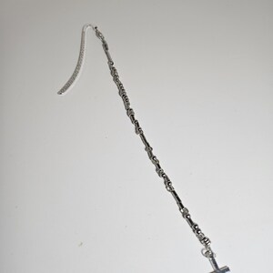 May include: A silver-colored bookmark with a cross charm. The bookmark features a chain design with a curved top for inserting into a book. The cross charm hangs at the bottom of the chain.