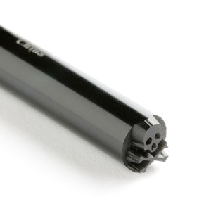 May include: A black, cylindrical stamp with a skull design at the end. The stamp is labeled "Caritas" on the side.