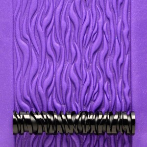 Könnte beinhalten: Eine violette, strukturierte Teigrolle mit einem schwarzen und silbernen Muster. Die Teigrolle wird verwendet, um ein strukturiertes Muster auf Fondant oder Ton zu erstellen.