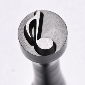 May include: A close-up of a metal stamp with a musical note design. The stamp is black and has a textured surface.