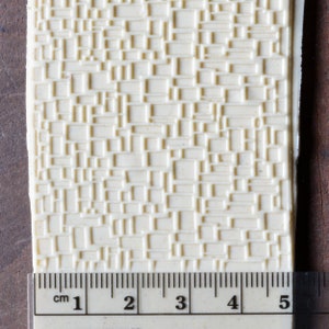 May include: A close-up of a white, textured silicone mold with a repeating pattern of squares. The mold is 5 cm wide and is measured with a ruler.