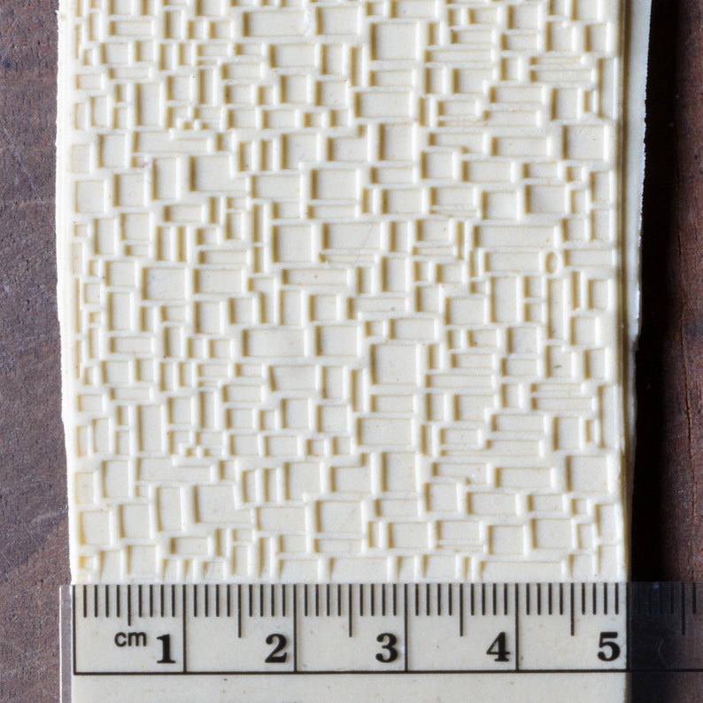 May include: A close-up of a white, textured silicone mold with a repeating pattern of squares. The mold is 5 cm wide and is measured with a ruler.