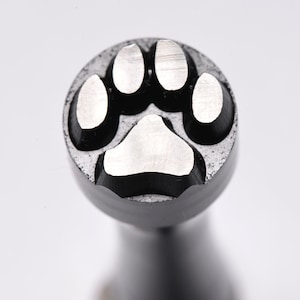 May include: Close-up of a metal paw print stamp. The stamp features a circular design with a detailed paw print impression. The paw print is made up of five distinct pads, with a textured background.