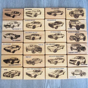May include: A collection of twenty rectangular wooden blocks arranged in a grid, each featuring a laser-engraved illustration of a specific vehicle model with its corresponding name printed in black text above or below the car image.