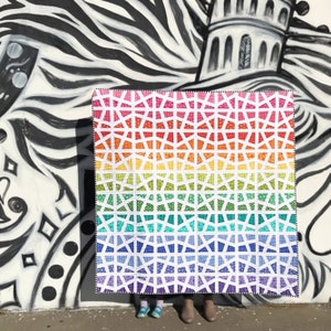 Puede incluir: Una colcha de colores arcoíris con un patrón geométrico. La colcha está hecha de cuadrados blancos con formas geométricas coloridas en su interior. La colcha está colgada en una pared con un patrón de cebra en blanco y negro.