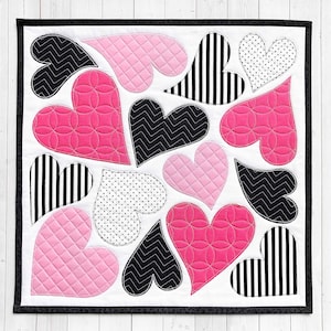 以下が含まれることがあります： 黒い縁取りのある白い布の正方形には、ピンクと黒のハートの寄せ集めが施されています。それぞれのハートは、ストライプ、水玉模様、ジグザグなど、異なるキルトパターンを持っています。