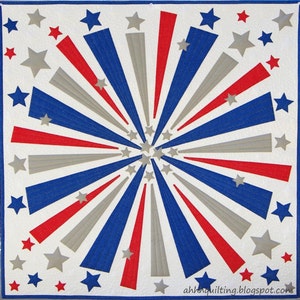 May include: A white quilt with a red, white, and blue starburst design. The quilt is made of fabric with a textured surface. The quilt is decorated with white stars.