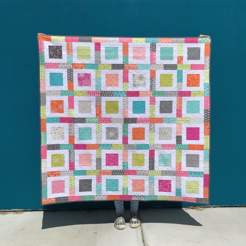 May include: A colorful quilt with a patchwork design featuring squares of various colors and patterns, including pink, green, blue, orange, and white. The quilt is made with a variety of fabrics and has a white border.