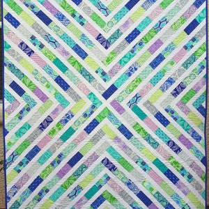 May include: A quilt with a chevron pattern in shades of blue, green, purple, and white. The quilt is made with a variety of fabrics and has a blue border.