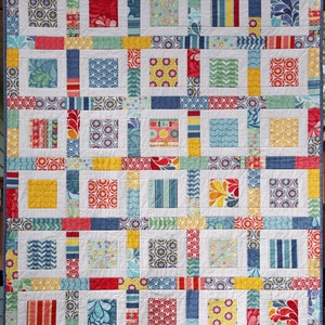May include: A colorful quilt with a patchwork design featuring squares of various colors and patterns, including red, yellow, blue, and green. The quilt is made up of smaller squares arranged in a grid pattern. The quilt is edged with a blue trim.