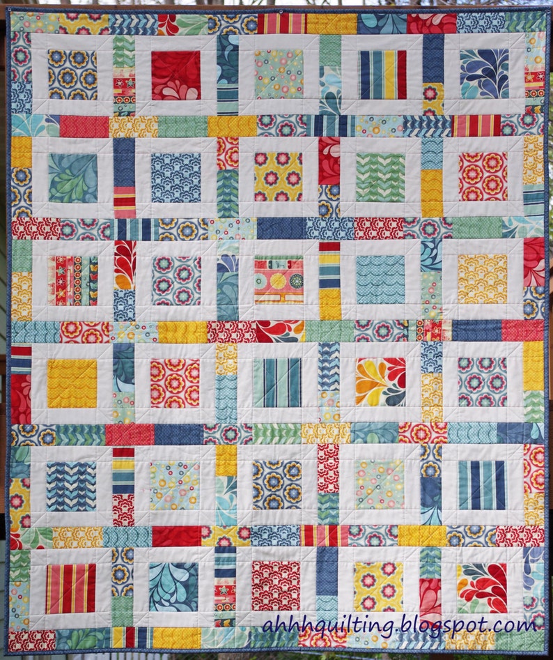 May include: A colorful quilt with a patchwork design featuring squares of various colors and patterns, including red, yellow, blue, and green. The quilt is made up of smaller squares arranged in a grid pattern. The quilt is edged with a blue trim.