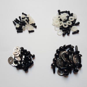 Può includere: Un assortimento di occhi di sicurezza e elementi di fissaggio in plastica nera per l'artigianato. L'immagine mostra quattro pile separate di occhi neri di varie dimensioni e stili, rondelle bianche e elementi di fissaggio neri, il tutto su sfondo bianco.