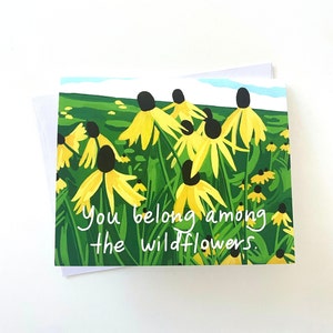 Puede incluir: Una tarjeta de felicitación con fondo verde y flores amarillas con centros negros. El texto "You belong among the wildflowers." está escrito en blanco en la tarjeta.