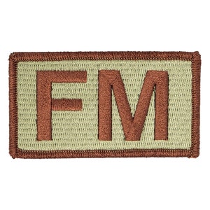 May include: A brown embroidered patch with the letters "FM" in a light tan color.
