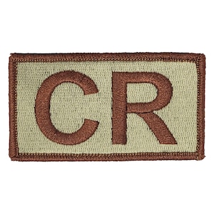 May include: A tan embroidered patch with a brown outline. The patch features the letters "CR" in brown.