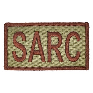 May include: A tan rectangular patch with a brown embroidered border and the word "SARC" in brown lettering.