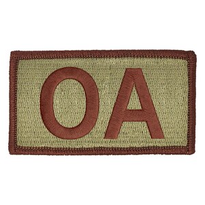 May include: Embroidered patch with the letters "OA" in a reddish-brown color. The letters are stitched onto a light green background, framed by a brown border. The patch has a rectangular shape.