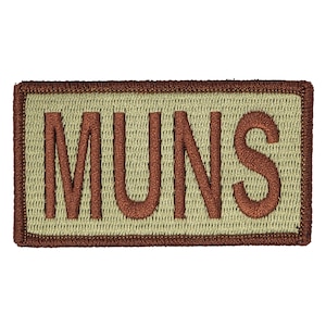 May include: A tan embroidered patch with brown stitching and the word "MUNS" in brown lettering.