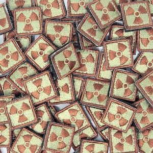 May include: A pile of small, square, green and brown patches with a stylized radiation symbol embroidered on each one.
