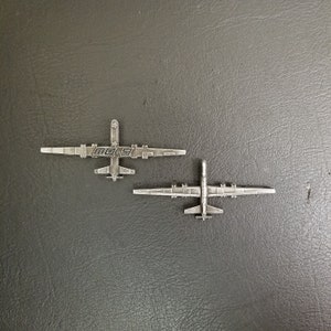May include: Two silver metal pins shaped like the MQ-9 Reaper drone. The top pin has the text "MQ-9" on it.