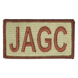 Peut inclure: Un écusson brodé beige avec une bordure marron. L'écusson porte l'inscription "JAGC" en lettres marron.