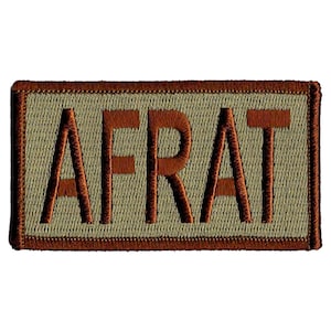 May include: Embroidered patch with the word "AFRAT" in brown capital letters. The letters are stitched onto a tan background, framed by a brown border. The patch has a rectangular shape.
