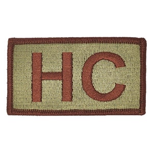 May include: A tan fabric patch with a brown embroidered border and the letters "HC" in brown.
