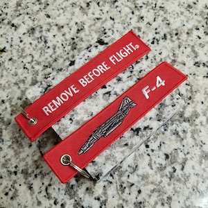 May include: Red keychain with a white embroidered airplane and the text "REMOVE BEFORE FLIGHT" on one side and "F-4" on the other side.