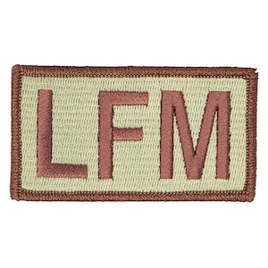 May include: A tan and brown embroidered patch with the letters "LFM" in brown.