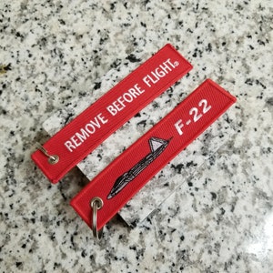 May include: Two red keychains with white text and a small airplane graphic. The top keychain says "REMOVE BEFORE FLIGHT." The bottom keychain says "F-22".