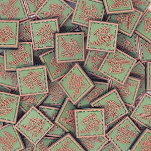 May include: A pile of green and orange square patches with a camouflage pattern and a stylized image of a person holding a rifle.