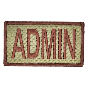 May include: A tan and brown rectangular patch with the word "ADMIN" embroidered in brown.